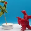 Flygon origami flying, and a Garchomp wax sculpture giving it a hand on a blue background